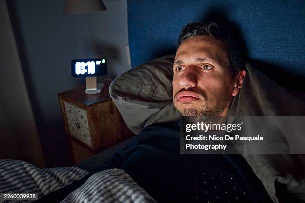 man awake in bed staring into space during sleepless night - digital clock face stock pictures, royalty-free photos & images