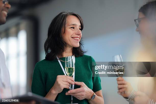 smiling woman in green at networking event with champagne glass and lanyard - champagne colored stock pictures, royalty-free photos & images