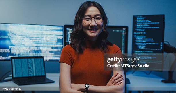 smiling asian female professionals confidently sit in front of computer with code on screen in office at night. portrait, working late, software developer, artificial intelligence and programming. - java code stock pictures, royalty-free photos & images