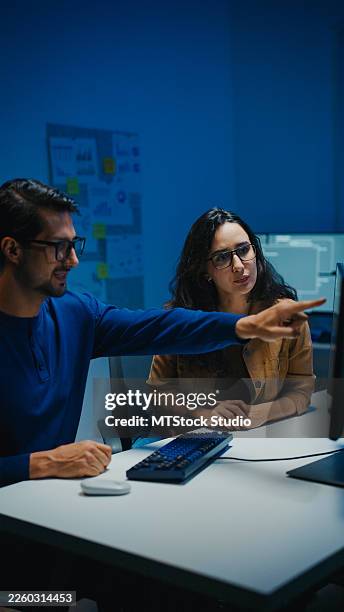 young latin software developers team meeting discussing source code on desktop monitor working late in dark office at night. artificial intelligence and programming concept. - software testing stock pictures, royalty-free photos & images