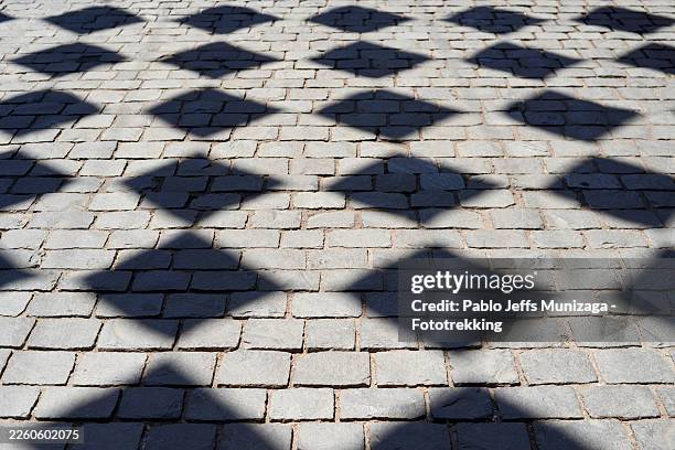 cobblestone pavement with repeated diamond shadows creating pattern - hårda material landskapsarkitektur bildbanksfoton och bilder