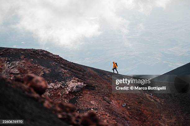 hiker in bright orange jacket ascending the volcanic slope of mount etna, sicily - paisaje volcánico fotografías e imágenes de stock