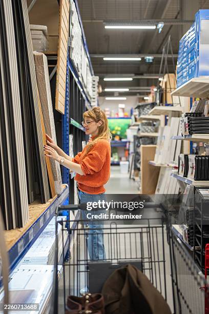 woman in orange sweater browsing building materials in a bright hardware store aisle - hardware store stock pictures, royalty-free photos & images