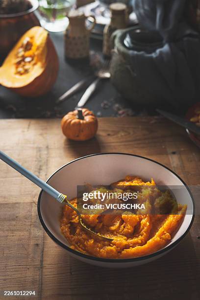 pumpkin puree in a bowl with a spoon on a rustic kitchen table. - pumpkin puree stock pictures, royalty-free photos & images