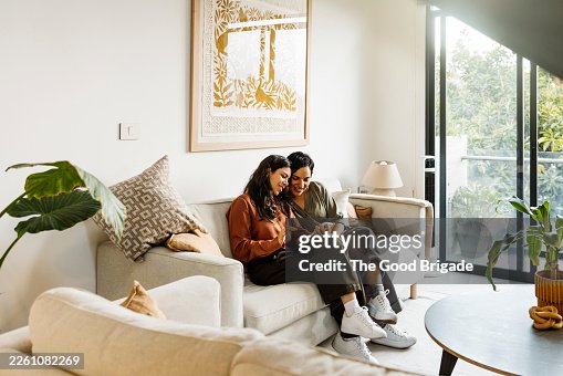 Lesbian couple using smart phone for video call while sitting on sofa Lesbian couple using smart phone for video call while sitting on sofa