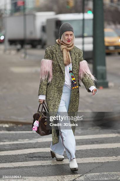 Person is seen wearing a grey knit beanie, tan fur scarf with a long pearl earring, yellow and black chevron-patterned overcoat with pink faux fur...