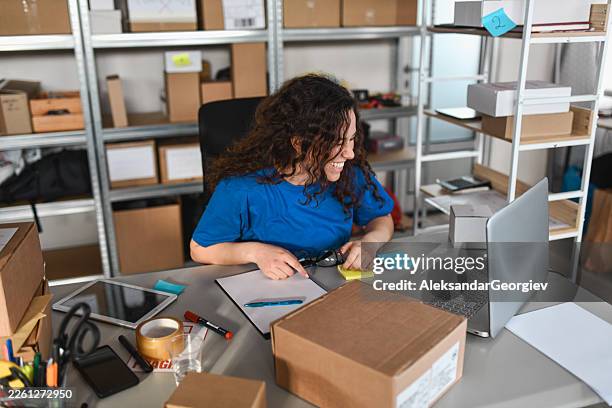 smiling female warehouse worker at desk with laptop and boxes in storage room - office supply stock pictures, royalty-free photos & images