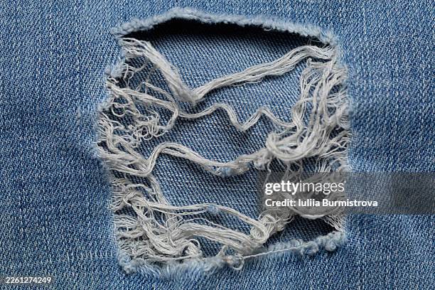 close-up of ripped blue jeans denim with frayed hole and distressed texture - ripped jeans stock pictures, royalty-free photos & images