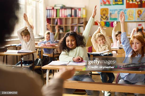 diverse students raising hands to answer teacher's question on a class. - criança de escola primária imagens e fotografias de stock