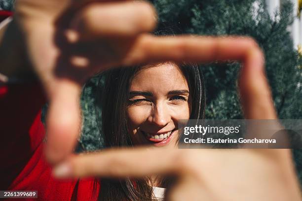 young woman framing winking face with fingers - focus stockfoto's en -beelden