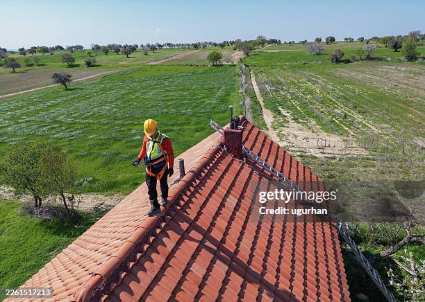 roofer walking on red tiled roof wearing safety harness - roof tile stock pictures, royalty-free photos & images