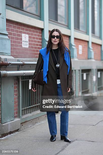 Annabel Rosendahl wears long dark brown hair, black rectangular sunglasses, a long silver pendant necklace with pink print pattern pendant, a dark...
