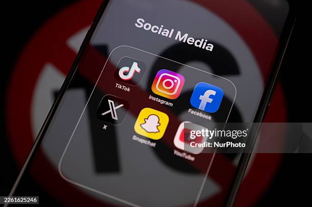 Social media logos display on a smartphone screen placed on a reflective surface onto which a symbol indicating an under-16 ban projects, as the...