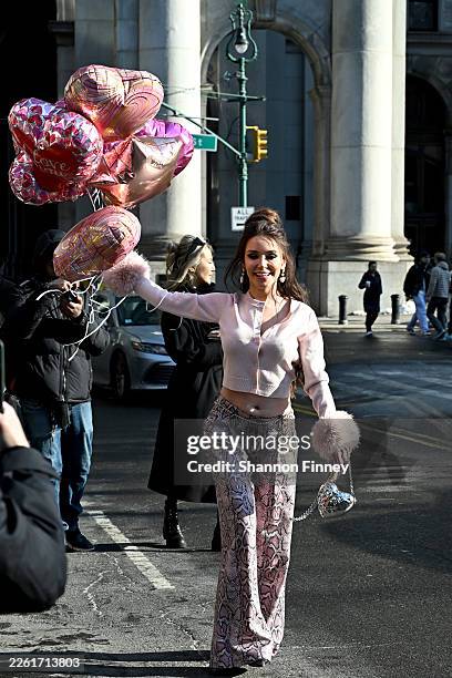 Nadiia Medvedchuk wears pink snakeskin print wide leg trousers a pink button-down sweater with faux fur cuffs while carrying Valentine's Day balloons...