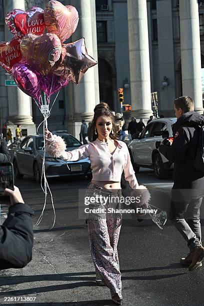Nadiia Medvedchuk wears pink snakeskin print wide leg trousers a pink button-down sweater with faux fur cuffs while carrying Valentine's Day balloons...