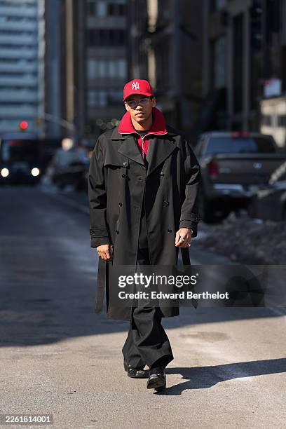 Guest wears a red baseball cap from New Era, black tinted glasses, a black long trench coat, a red knit high neck sweater, black straight-leg pants,...