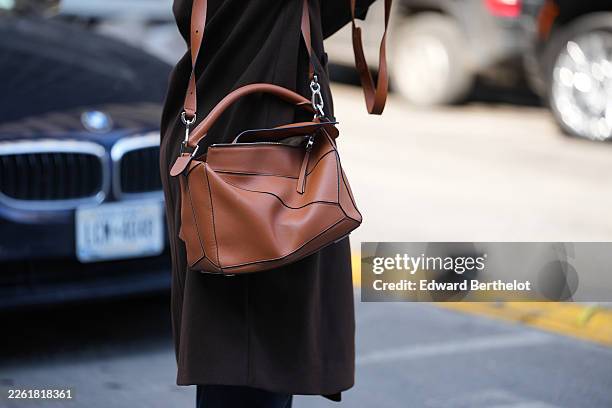 Guest wears a brown leather Puzzle handbag from Loewe, a black coat, outside Altuzarra, during New York Fashion Week, on February 14, 2026 in New...