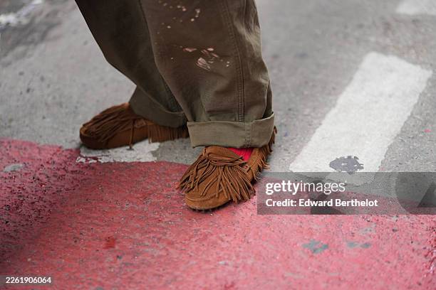 Guest wears olive paint-splatter straight-leg pants, brown suede fringed moccasin shoes, red socks, outside Diotima, during New York Fashion Week, on...