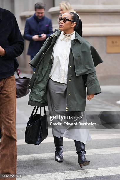 Guest wears black hair in a ponytail, black acetate oversized sunglasses, earrings, a black embossed crocodile pattern varnished leather bag, a green...