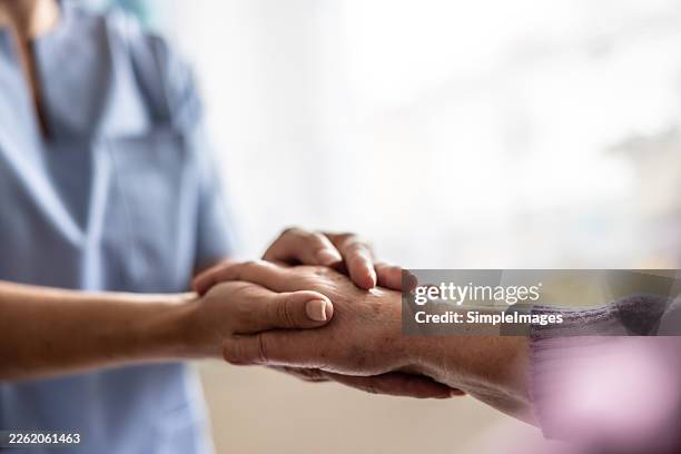 a close-up of a nurse in a blue uniform holding the hand of an elderly person with compassion. this moment exudes a strong sense of support, humanity, and care in a healthcare setting or retirement home. - servicios sociales fotografías e imágenes de stock