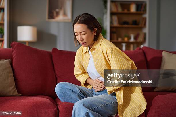 young asian woman experiencing stomach pain at home - autoimmune disease stock pictures, royalty-free photos & images