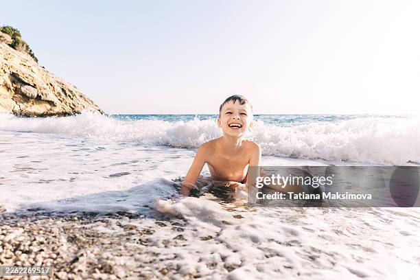a little boy is having fun on a sandy beach, enjoying the spray of the sea water. - badkläder bildbanksfoton och bilder