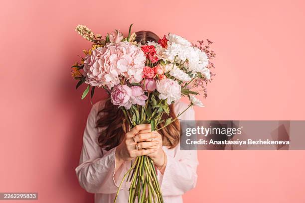 woman hiding face behind big flower bouquet on pink background, romantic concept - dankbarkeit stock-fotos und bilder