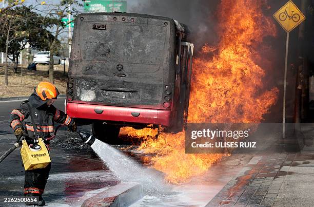 Firefighter extinguishes a burning bus set on fire by organised crime groups in response to an operation in Jalisco to arrest a high-priority...