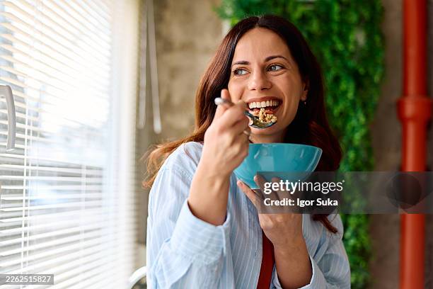 happy mid adult woman eating healthy breakfast bowl - muesli stock pictures, royalty-free photos & images