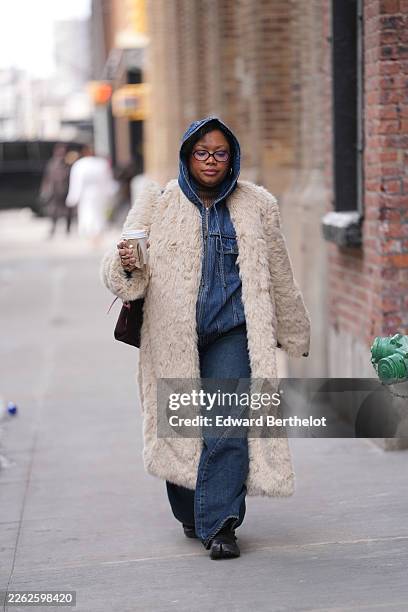 Guest wears a blue denim hood, black oval eyeglasses, gold earrings, a red burgundy leather shoulder bag, a beige faux fur long coat, a blue denim...