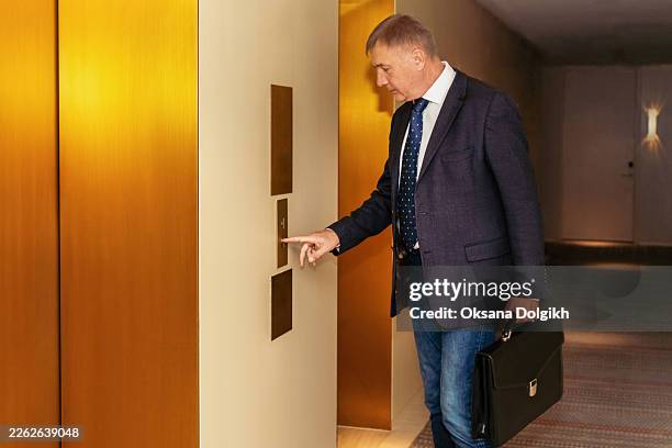 businessman presses elevator button in office building corridor during workday - pressing elevator button stock pictures, royalty-free photos & images