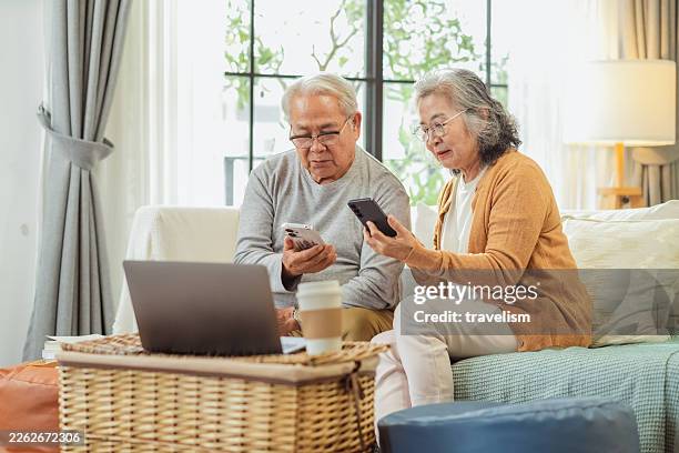 old senior married couple sit on sofa at home using smartphone to study and practice ai voice assistant and chatbot agent, asking questions together, exploring daily technology learning with joy and curiosity - question time stock pictures, royalty-free photos & images