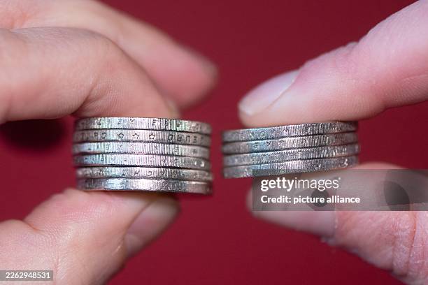 February 2026, Saxony, Dresden: A man and a woman hold stacked two-euro coins between their thumb and forefinger. Photo: Sebastian Kahnert/dpa
