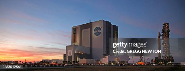 Mobile launcher 1 containing the massive Artemis II Space Launch System rocket and Orion spacecraft rolls back from Launch Complex 39B towards the...