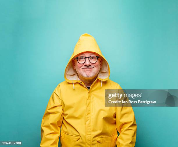 man making funny face wearing yellow raincoat with hood - raincoat stock pictures, royalty-free photos & images