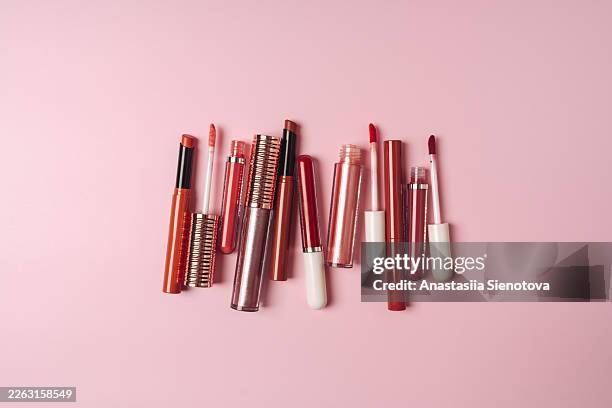 variety of lipstick and lip gloss tubes on pink background for makeup and cosmetics flat lay - lip gloss stock pictures, royalty-free photos & images