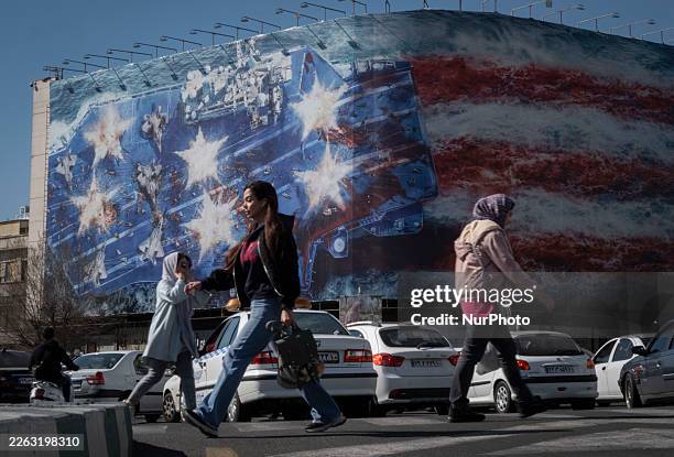 Young Iranian women walk past a state building covered with a giant anti-U.S. Billboard depicting a symbolic image of the destroyed USS Abraham...