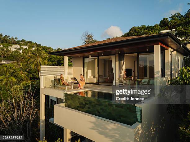 women relaxing by infinity pool at luxury villa - wide shot stock pictures, royalty-free photos & images