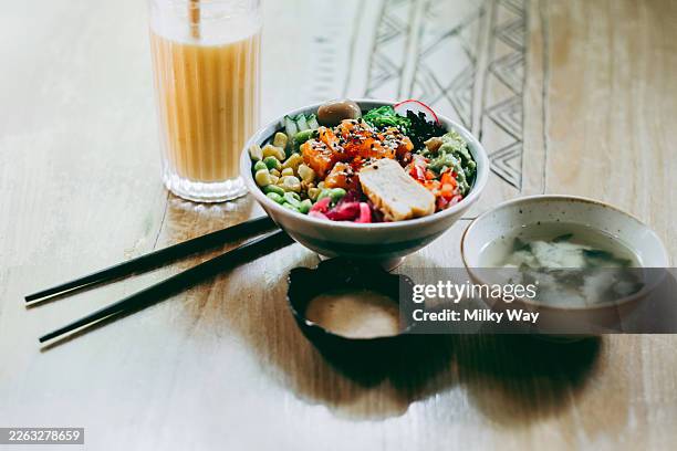 bowl with colorful vegetables, tofu and salmon. glass of latte and bowl of soup on wooden table. natural light and soft shadows. food photography with warm tones. concept of balanced meal and healthy lifestyle. - nori photos et images de collection
