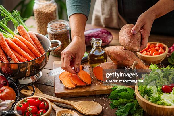 unrecognizable person preparing fresh organic sweet potato in the kitchen. woman cooking root vegetables for a vegetarian meal. healthy eating or dieting for wellbeing - zoete aardappel stockfoto's en -beelden