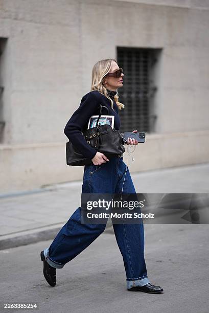 Mirja Klein is seen wearing a navy fine knit turtleneck sweater with long sleeves and a fitted silhouette from COS; dark wash baggy jeans with a...