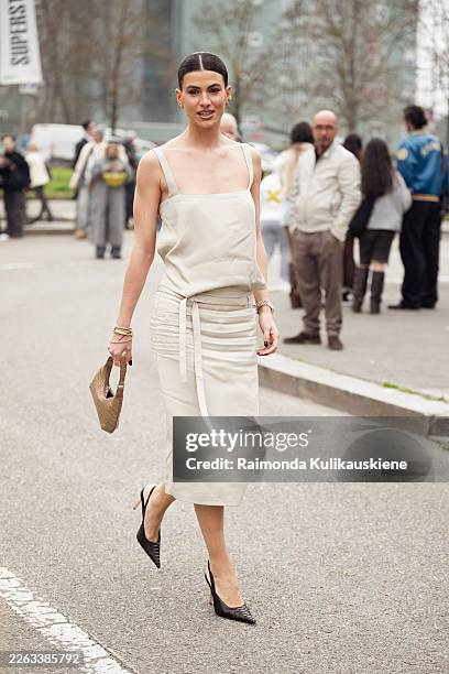 Guest wears a minimalist beige sleeveless camisole with thin straps tucked into a matching high-waisted midi skirt featuring soft ruching and a...