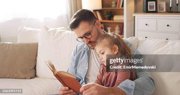 father reading book to young daughter at home - modern manhood stock pictures, royalty-free photos & images