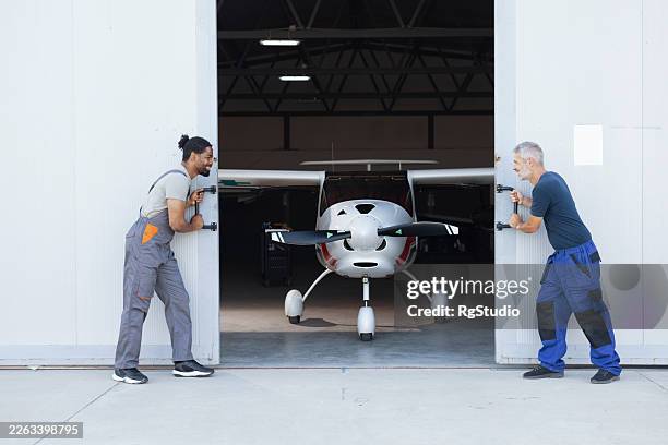 mechanics opening hangar doors pulling airplane outside - opening hangar stock pictures, royalty-free photos & images