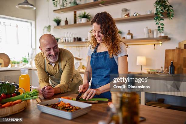 couple cooking together in a bright home kitchen as wife teaches husband to prepare a meal - casserole stock pictures, royalty-free photos & images
