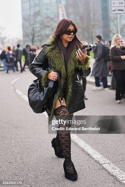 Guest wears dark brown hair, black sunglasses, a black varnished leather long coat with dark green faux fur trim, a dark purple knit top, black lace...