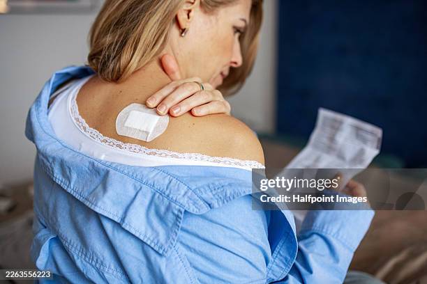 woman looking at medical leaflet after applying vaccine patch on shoulder. - menopause stock pictures, royalty-free photos & images
