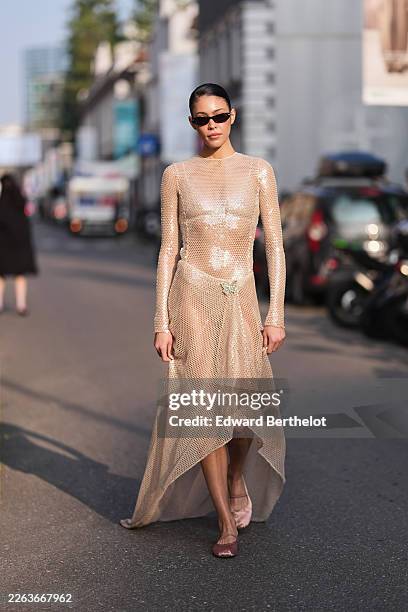 Guest wears black hair in a bun, black cat eyes sunglasses, a beige mesh / fishnet with embroidered white sequin fitted long sleeve top, a matching...