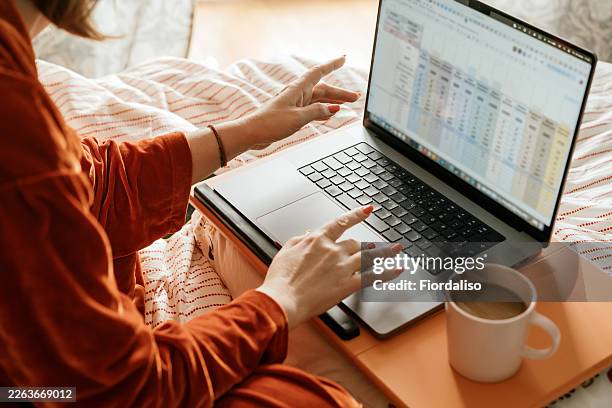 woman working from home on laptop in bed with coffee and spreadsheet open - spreadsheet stock pictures, royalty-free photos & images