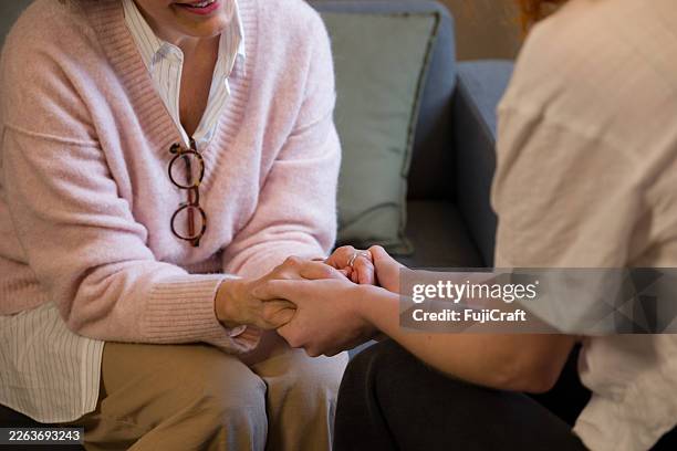 senior adult and young adult holding hands offering emotional support - perdão imagens e fotografias de stock